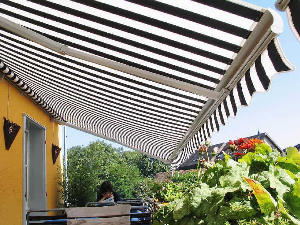 Auvent rayé noir et blanc ombrageant un patio avec une personne et des plantes.