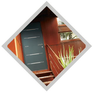 Porte grise avec lignes horizontales, escaliers et balustrade contre un bâtiment rouge.