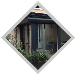 Fenêtres et porte à cadre noir d'un immeuble, vues à travers un losange. Des plantes sont visibles au premier plan.