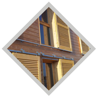 Façade en bois avec plusieurs fenêtres et volets clairs. Un rail métallique longe la partie inférieure.