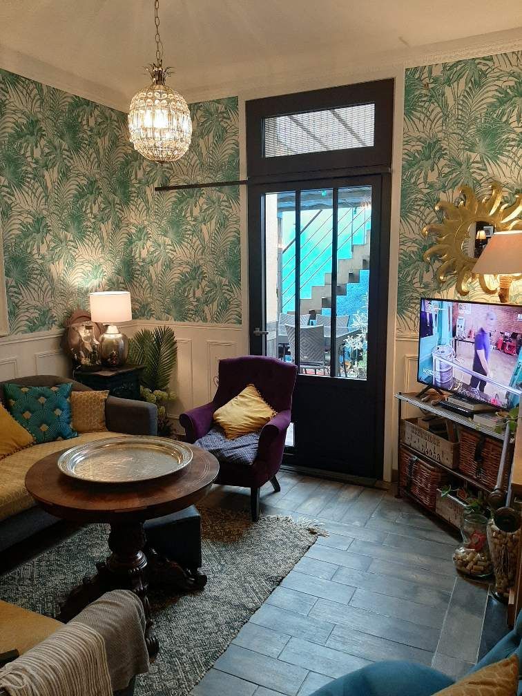 Salon avec papier peint à motifs bleu sarcelle, fauteuil violet et table ronde en bois.