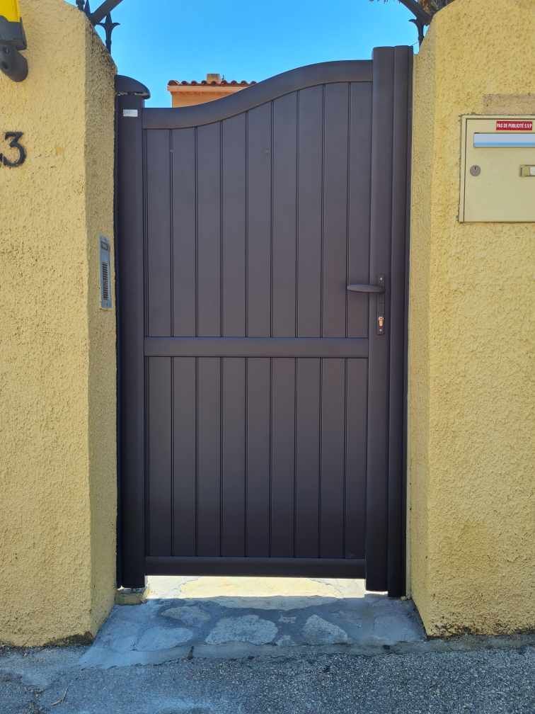 Portail marron foncé situé entre deux murs en stuc jaune.