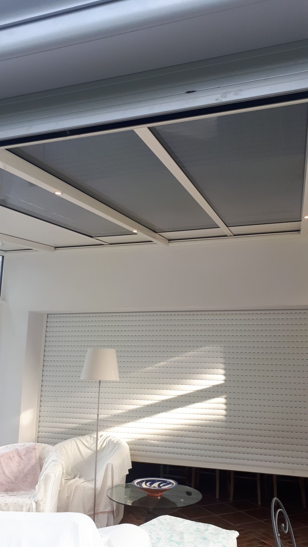 Intérieur avec stores blancs, plafond blanc avec puits de lumière et lampe.