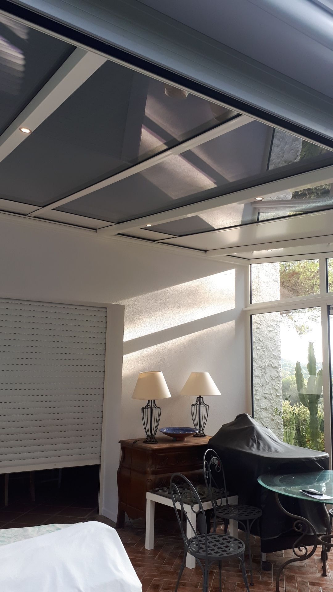 Intérieur de véranda avec un toit translucide, des murs blancs et des meubles d'extérieur.