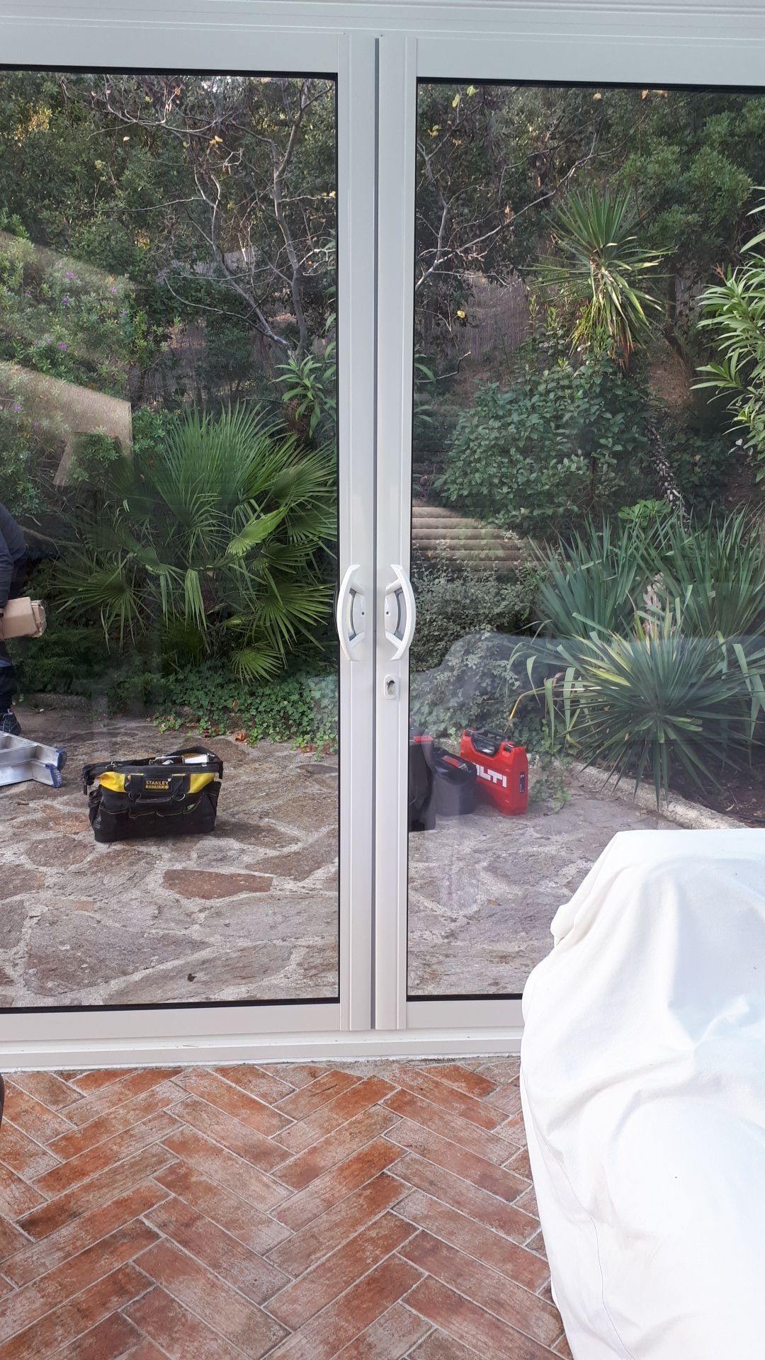 Portes vitrées ouvrant sur un jardin, avec des outils et une personne visibles à l'intérieur.