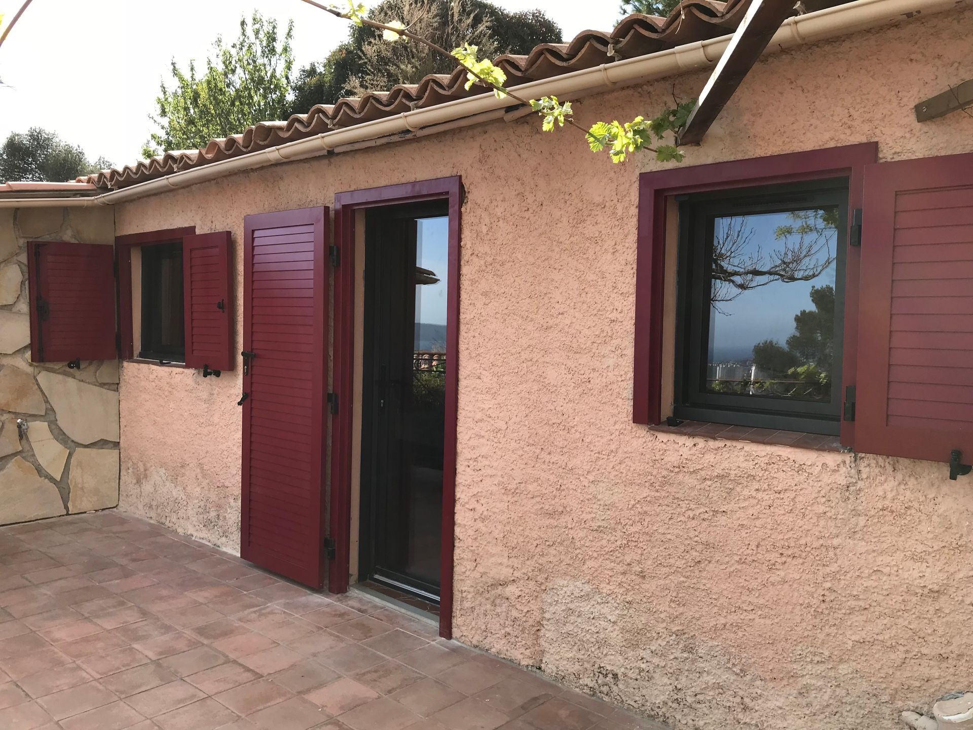 Extérieur d'un bâtiment avec volets et porte rouges, situé sur un patio.