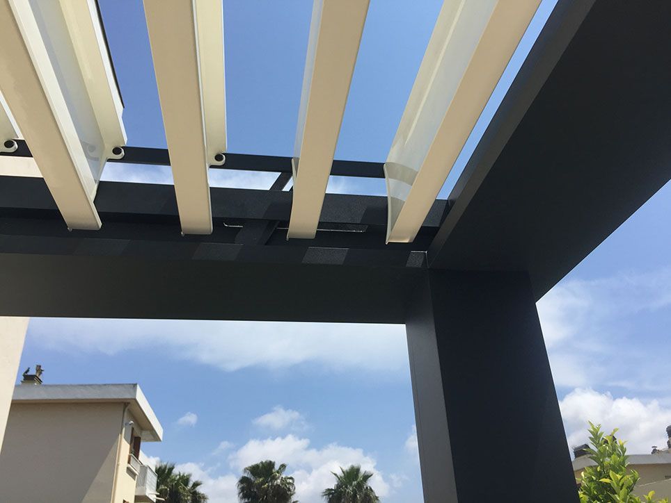 Toit de pergola avec des lattes de couleur crème sur fond de ciel bleu, soutenu par des poutres gris foncé.