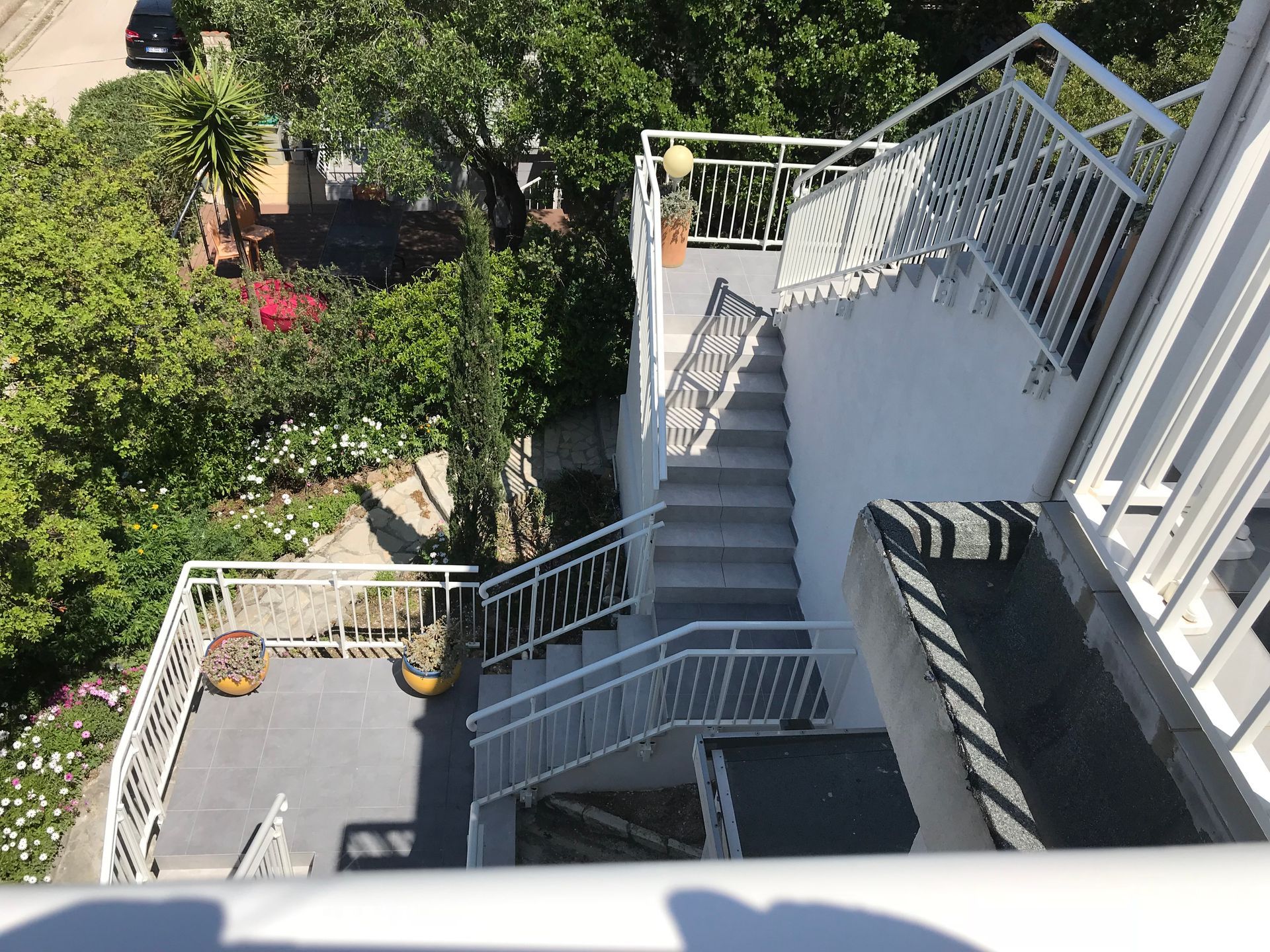 Un escalier avec des rampes blanches mène à une terrasse sur le toit, entourée d'arbres verts luxuriants.