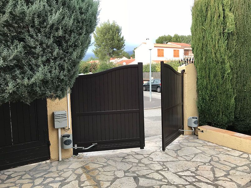 Portail automatique marron partiellement ouvert, donnant sur une rue avec maisons et arbres.