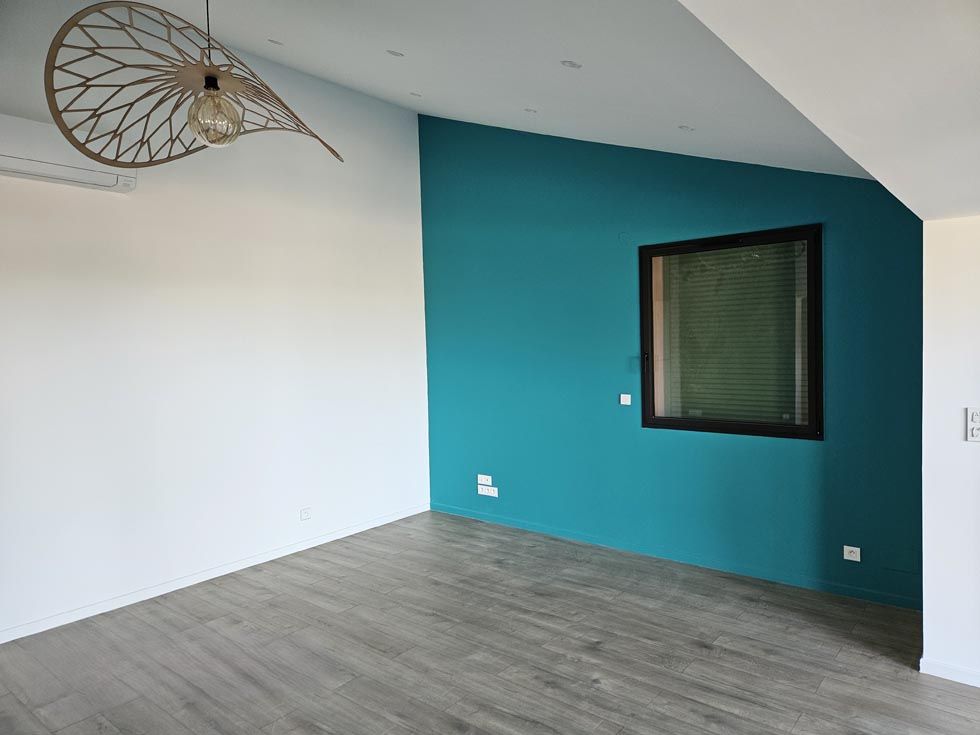 Pièce vide avec murs blancs et bleu sarcelle, parquet, fenêtre et luminaire décoratif.