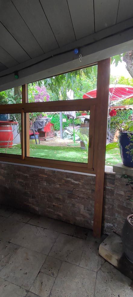 Vue depuis un patio couvert regardant à travers des cadres de fenêtres en bois vers un jardin avec un parasol rouge.