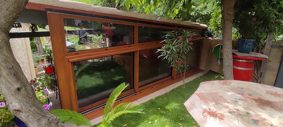 Un jardin avec une longue fenêtre à cadre en bois, des plantes et une petite table.