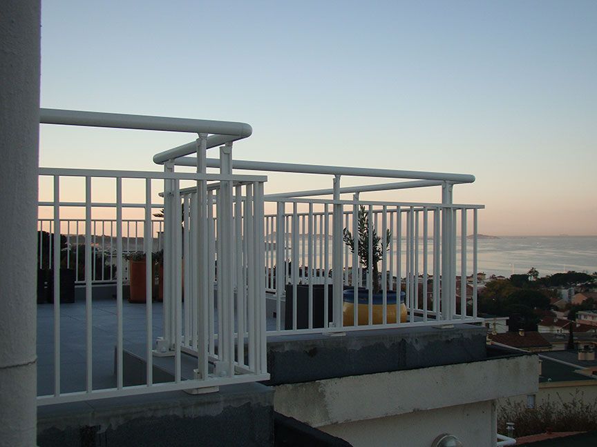 Balustrade blanche sur un toit surplombant l'océan au coucher du soleil.