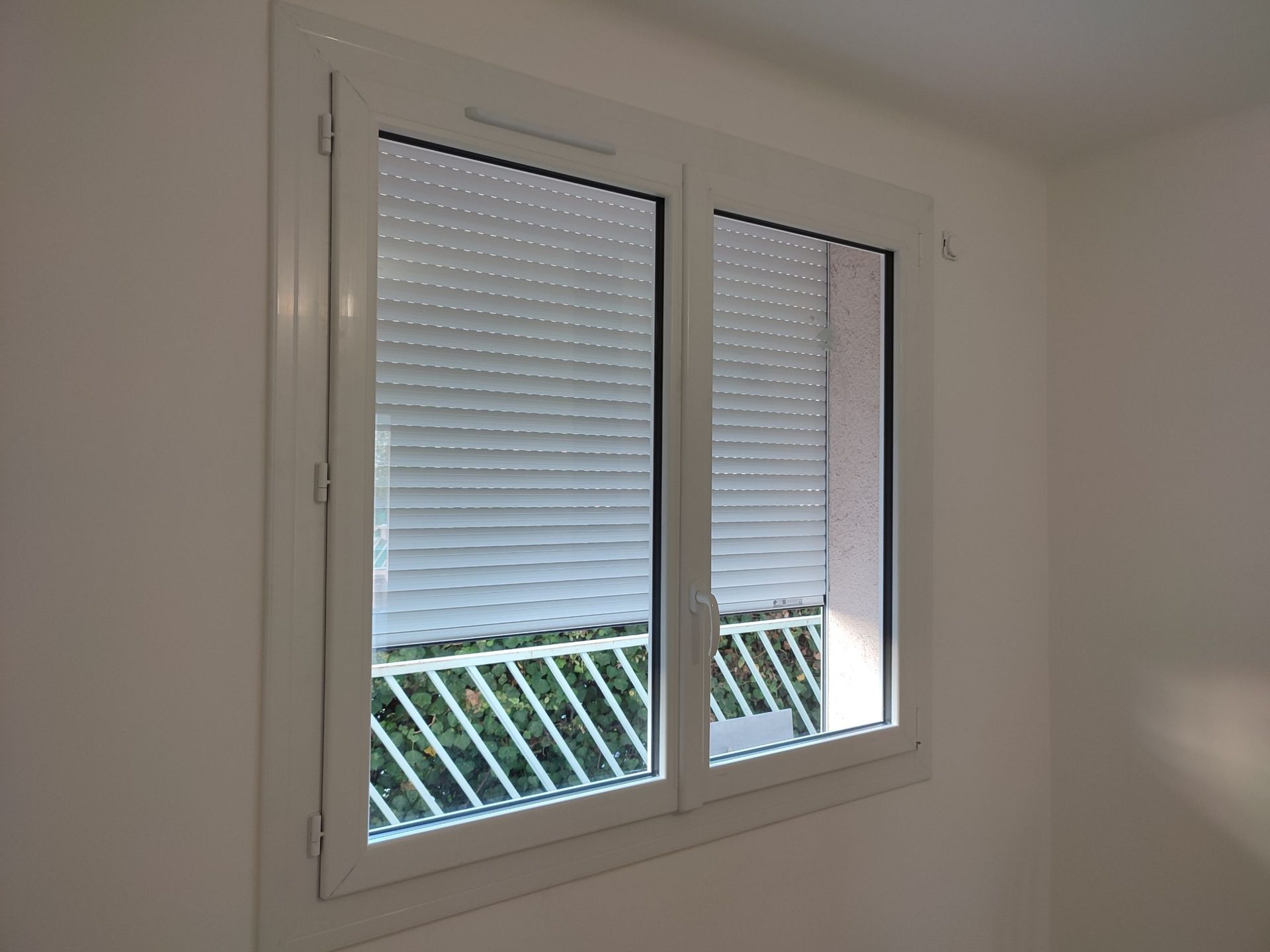 Fenêtre blanche avec stores fermés, donnant sur un balcon blanc.