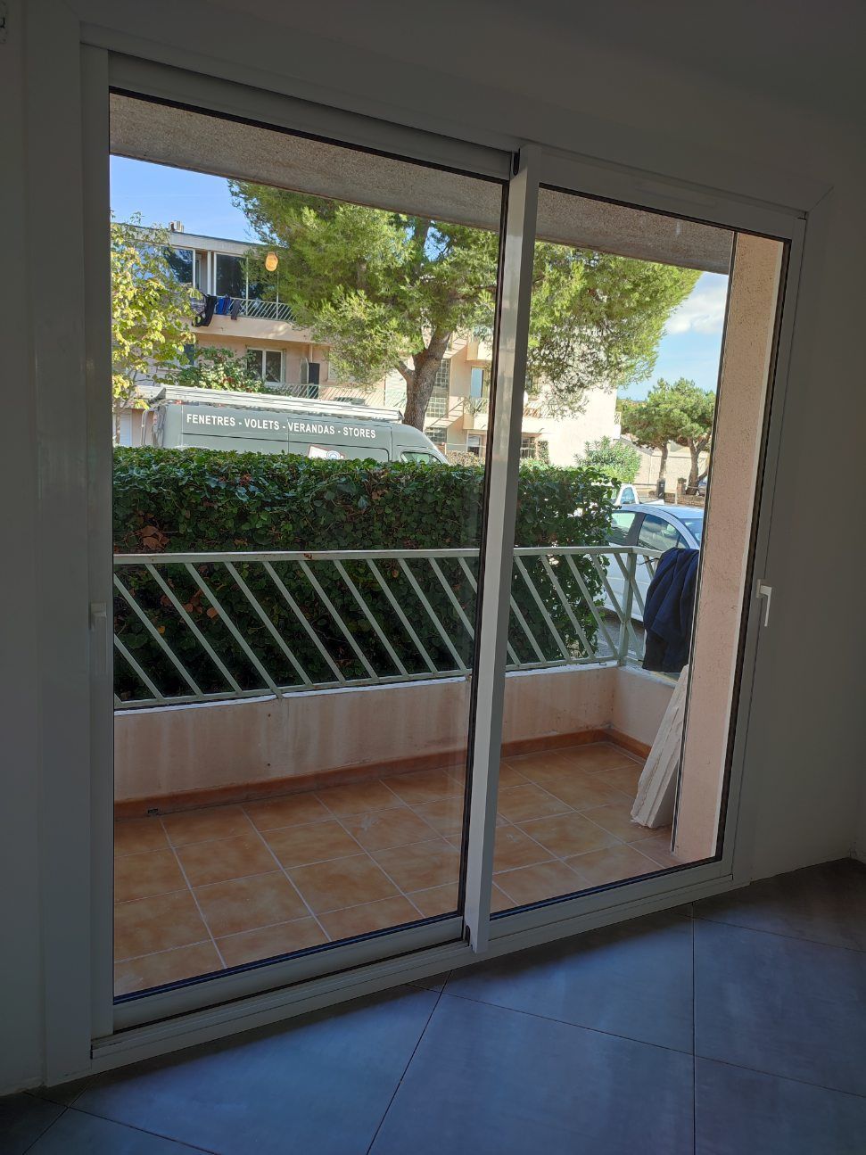 Porte coulissante en verre donnant sur un balcon avec feuillage vert et balustrade à l'extérieur.