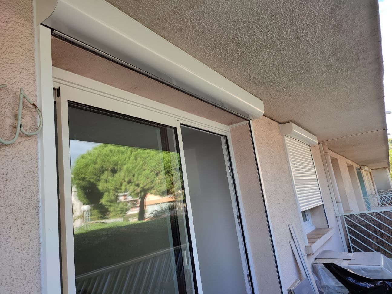 Volet roulant blanc au-dessus d'une porte coulissante en verre sur un mur extérieur.