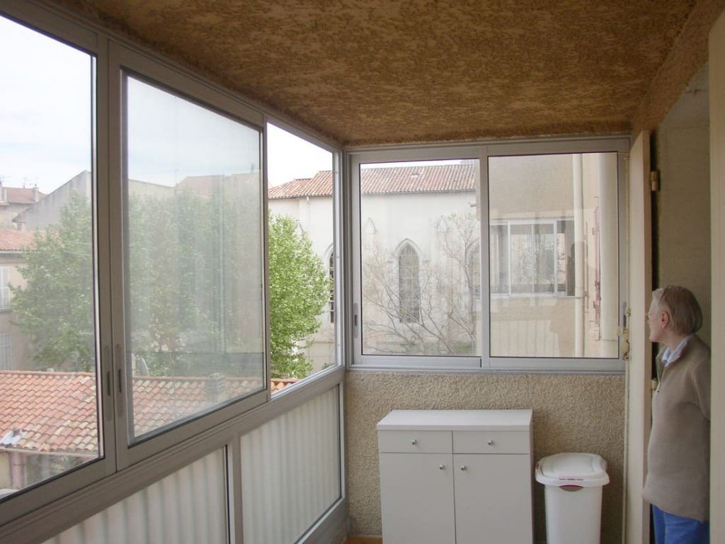 Balcon fermé avec fenêtres, une armoire et une personne regardant à l'extérieur.