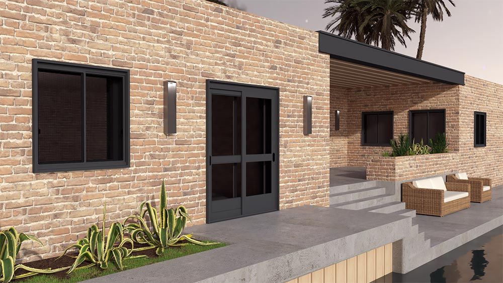 Bâtiment moderne en briques avec fenêtres et porte noires, sièges extérieurs et verdure.