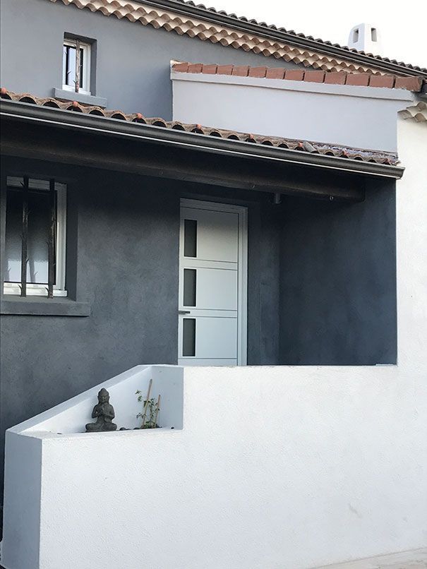 Extérieur d'une maison grise et blanche avec une porte bleu clair, des marches et une petite statue de Bouddha.