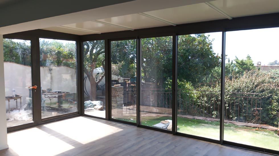 Véranda avec grandes baies vitrées donnant sur une cour arrière avec arbres et mur de béton.