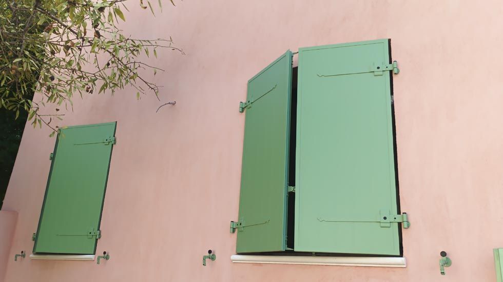 Volets verts sur un bâtiment rose ; un volet est ouvert.