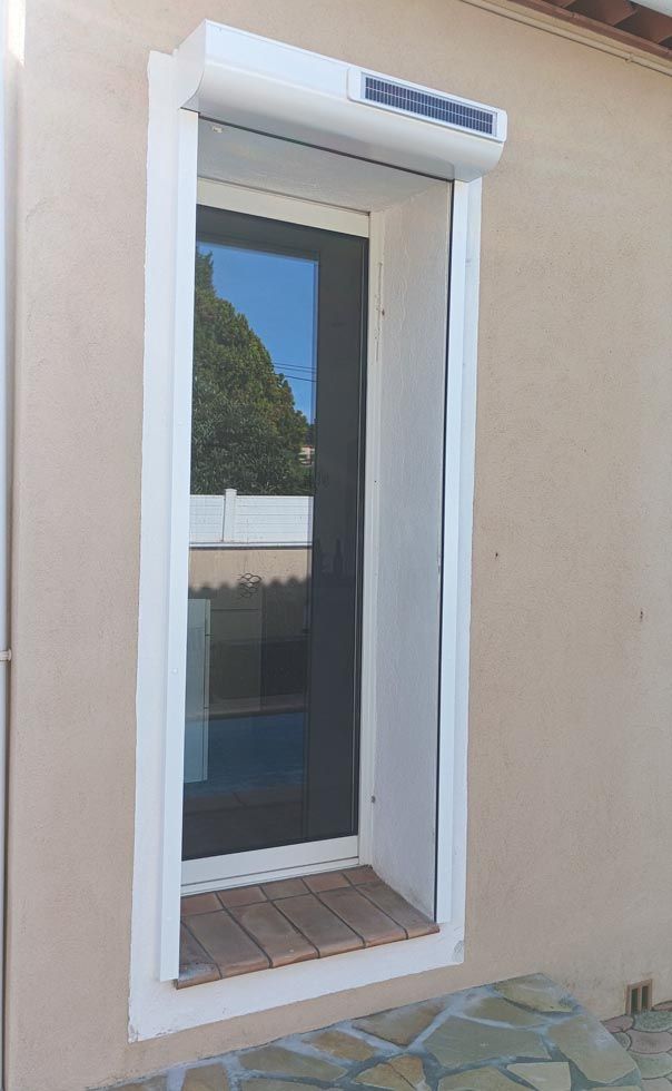 Fenêtre avec volet solaire blanc. La fenêtre est encastrée dans un mur beige.