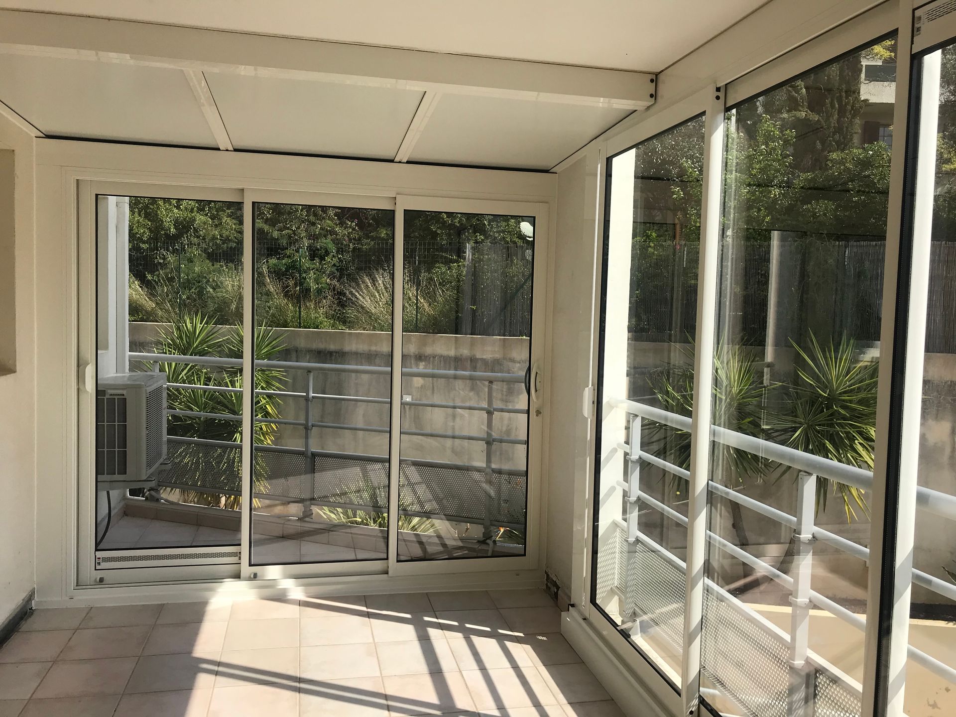 Véranda avec portes coulissantes en verre, murs blancs et vue extérieure.