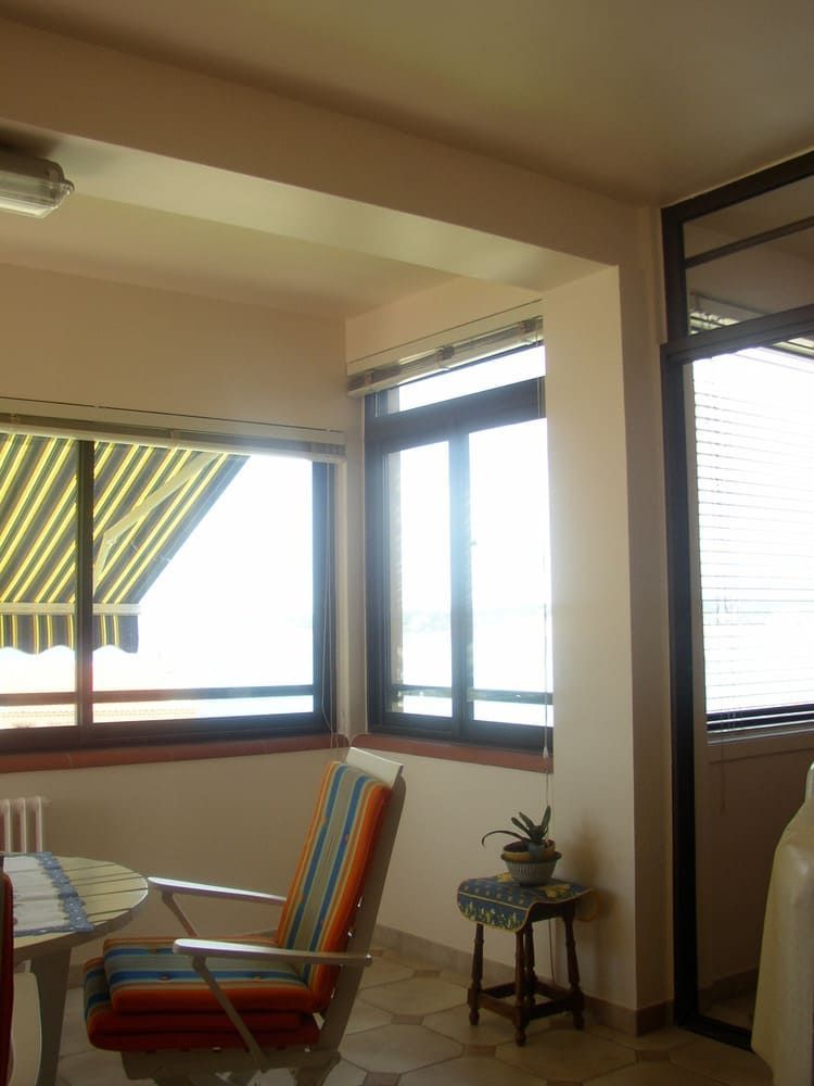 Intérieur avec fenêtres, chaise, table et support pour plantes. La lumière du soleil entre à flots.