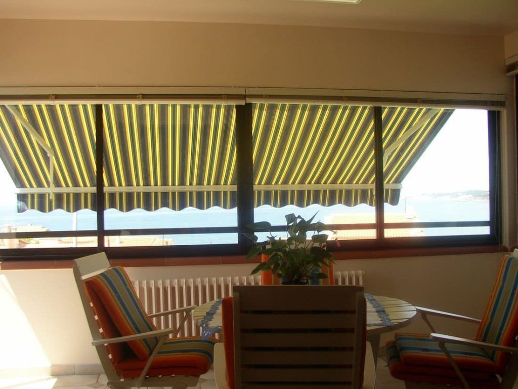 Balcon avec auvents rayés, vue sur l'océan, table, chaises.