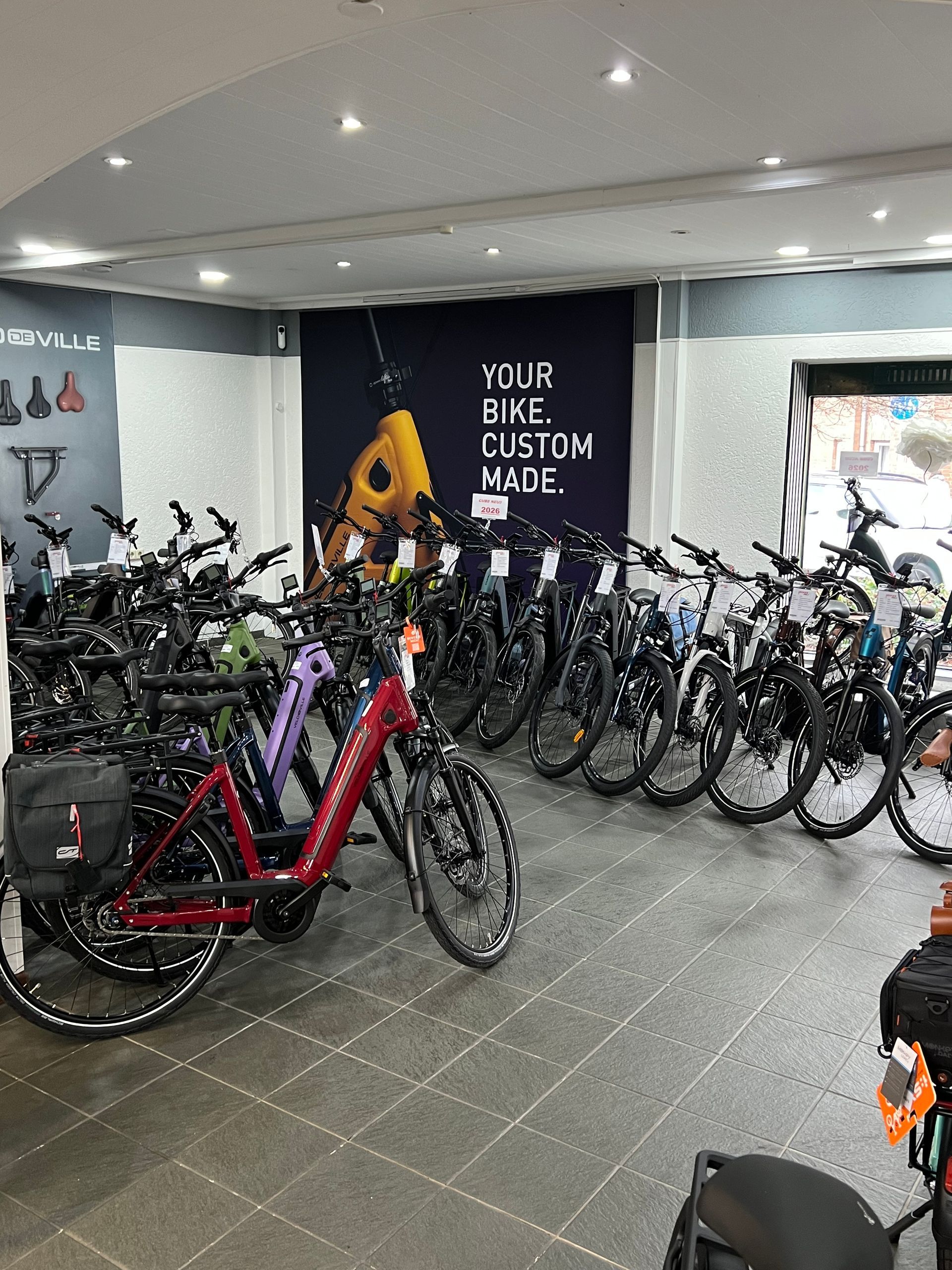 Innenansicht eines Fahrradgeschäfts mit vielen ausgestellten Fahrrädern. Ein Schild verkündet: „IHR FAHRRAD INDIVIDUALISIERT“.