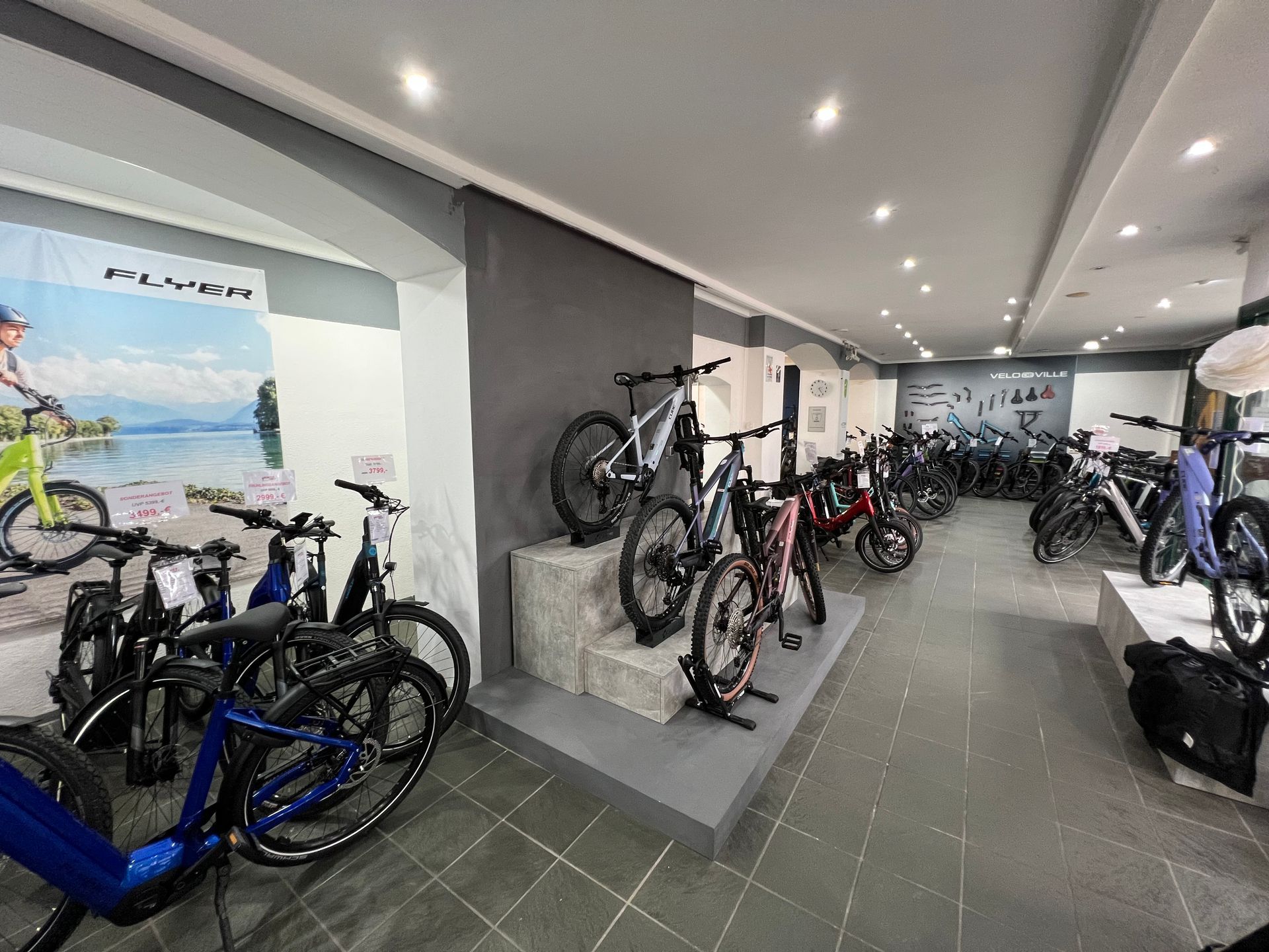 Innenraum eines Fahrradgeschäfts mit verschiedenen ausgestellten E-Bikes. Graue, schwarze und rote Fahrräder heben sich von einem hellen, neutralen Hintergrund ab.