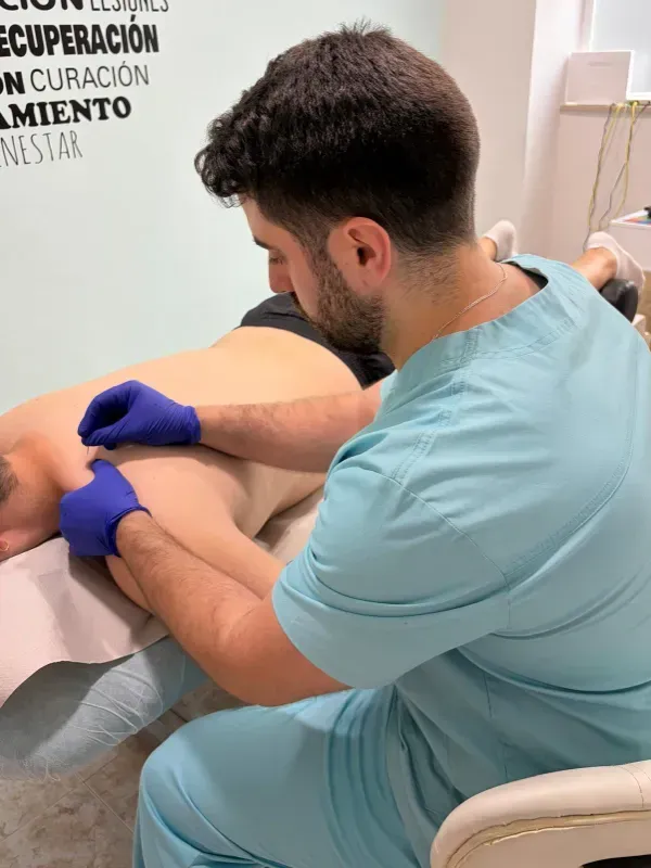 Un clínico con uniforme azul realiza un tratamiento de espalda a un paciente en una sala de consulta.