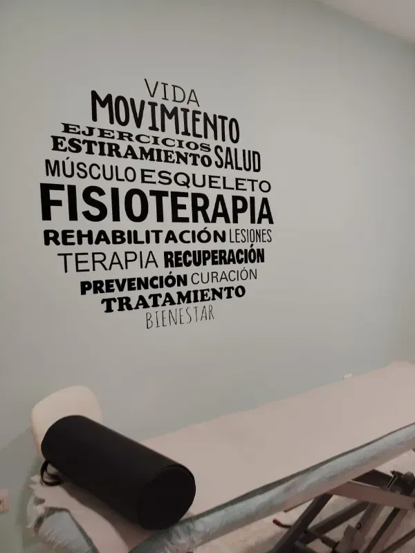 Camilla de tratamiento junto a un vinilo decorativo con palabras en español relacionadas con la rehabilitación y el fitness.