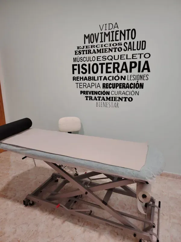 Camilla de rehabilitación en una sala de consulta con texto mural en español sobre salud y terapia.