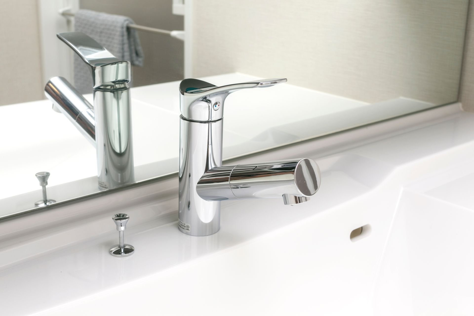 Robinet chromé sur un lavabo blanc, avec un miroir derrière. Serviettes grises sur un porte-serviettes à proximité.