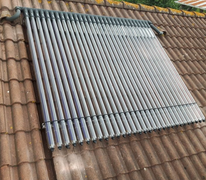 Tubes solaires thermiques installés sur un toit en tuiles brunes, captant la lumière du soleil pour générer de la chaleur.