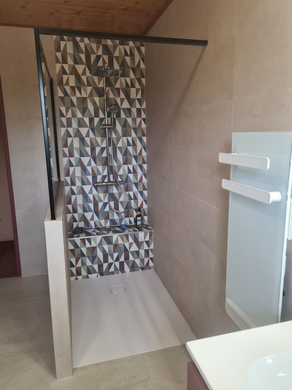 Douche avec mur en carrelage géométrique, sol de couleur claire et porte-serviettes mural blanc.