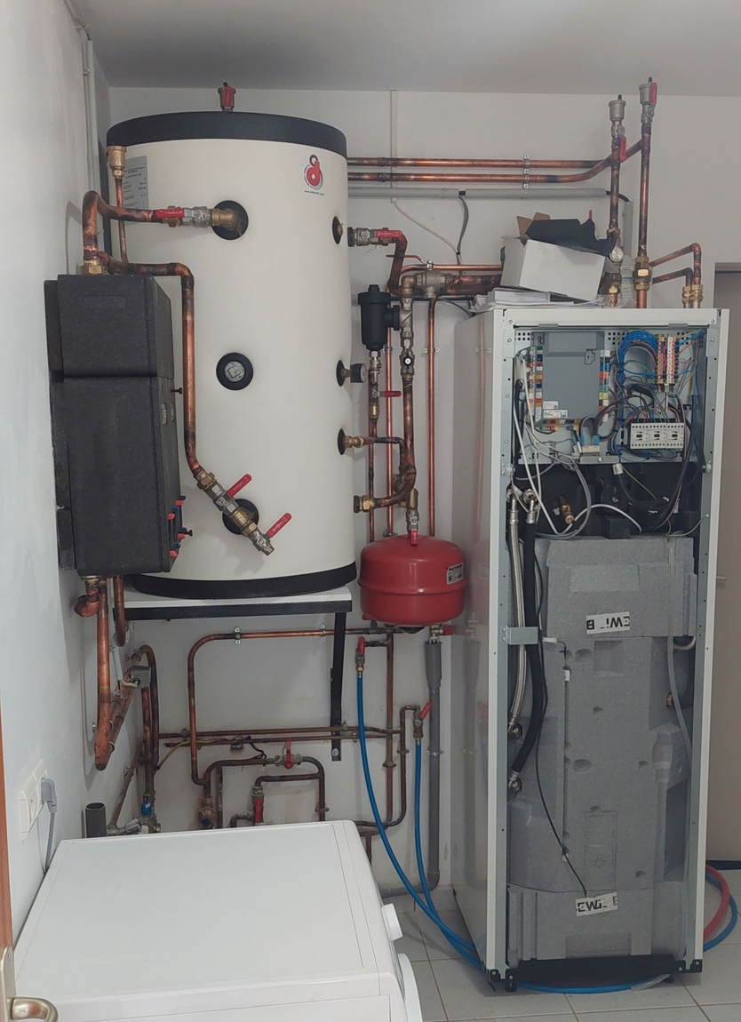 Système de chauffage avec réservoir d'eau, tuyaux et panneau de commande dans une pièce blanche.