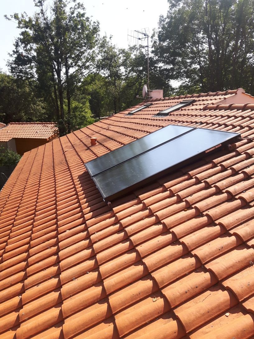 Panneau solaire sur un toit de tuiles rouge, arbres en arrière-plan, journée ensoleillée.
