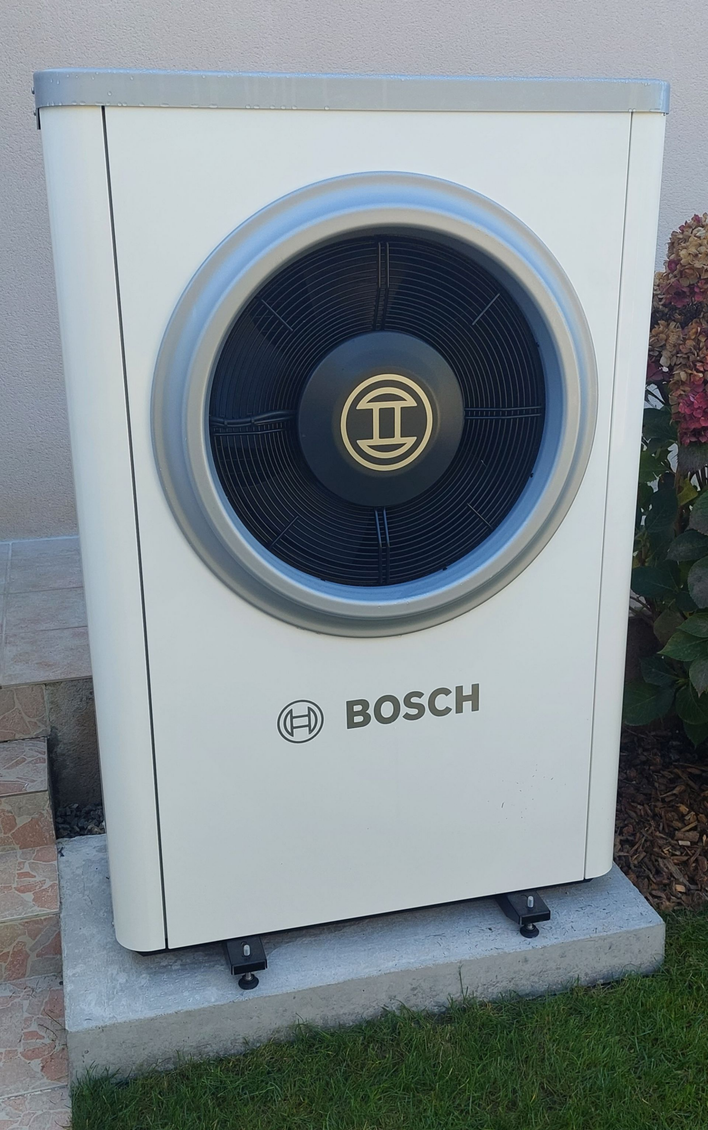Unité de pompe à chaleur à air Bosch blanche, montée sur une dalle de béton, à l'extérieur d'un bâtiment.