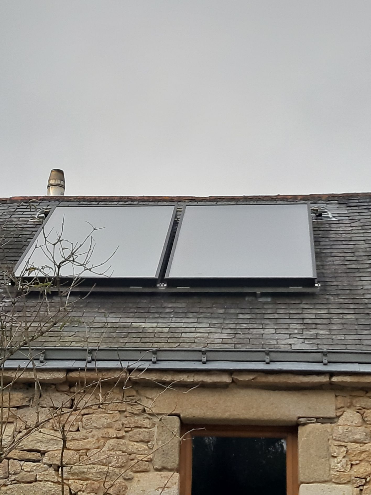 Panneaux solaires sur un toit en ardoise grise d'un bâtiment en pierre par temps nuageux.