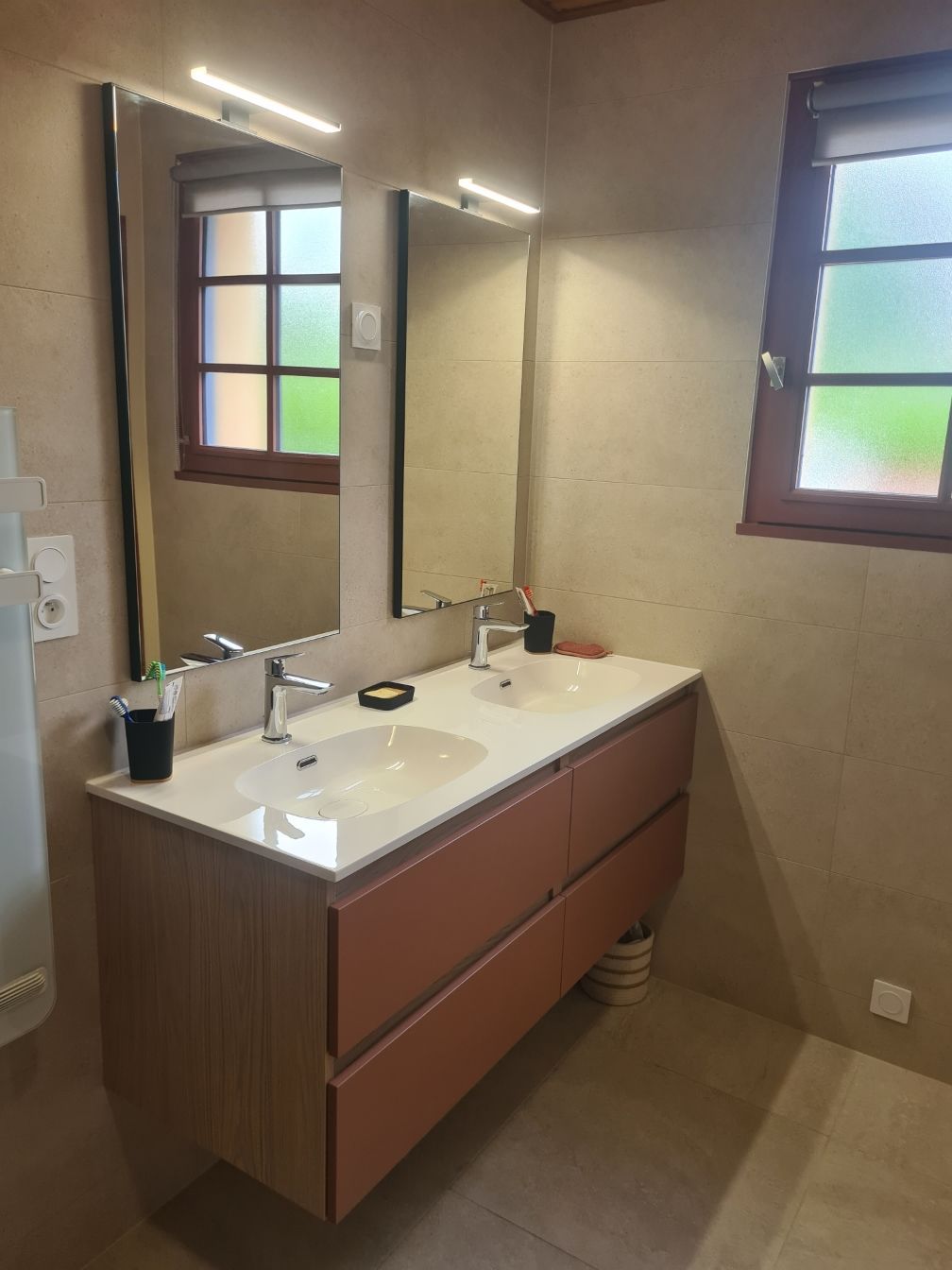 Salle de bains avec meuble-lavabo double, miroirs et fenêtres. Le meuble-lavabo  avec un plan de travail blanc.