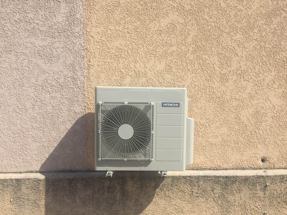 Unité de climatisation extérieure rectangulaire beige Hitachi, montée sur un mur extérieur texturé.