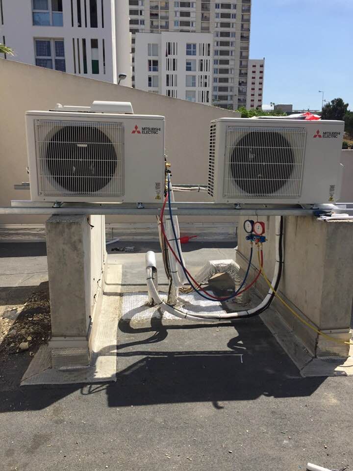 Deux unités de climatisation Mitsubishi blanches, montées sur des piliers en béton à l'extérieur, avec des manomètres.