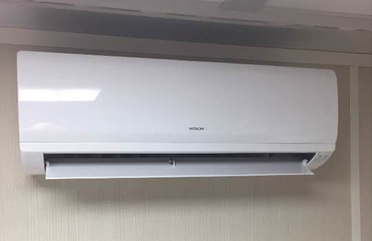 Un climatiseur mural Hitachi blanc, positionné près du plafond contre un mur neutre.