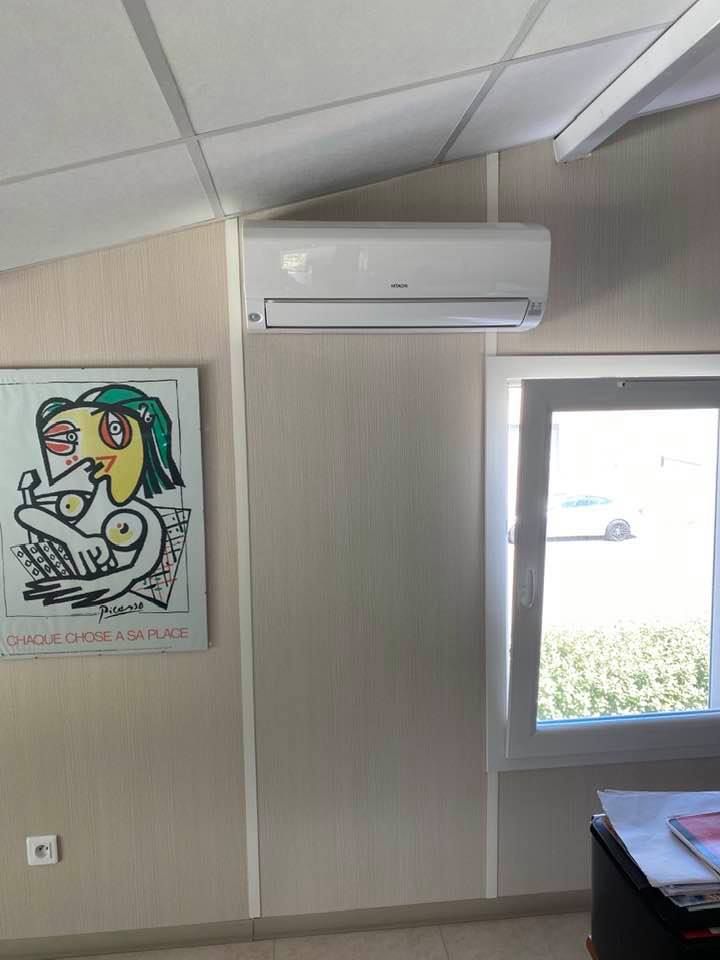 Un climatiseur mural blanc est placé au-dessus d'une fenêtre, à côté d'un tableau coloré encadré de style cubiste.