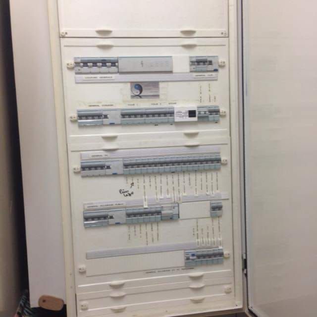 Tableau de distribution électrique ouvert, fixé au mur, comportant des rangées de disjoncteurs et d'interrupteurs.