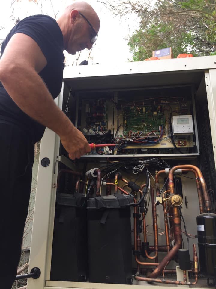 Un technicien pointe un outil vers le circuit interne d'une unité de climatisation extérieure ouverte, exposant ainsi ses tuyaux électriques et en cuivre.