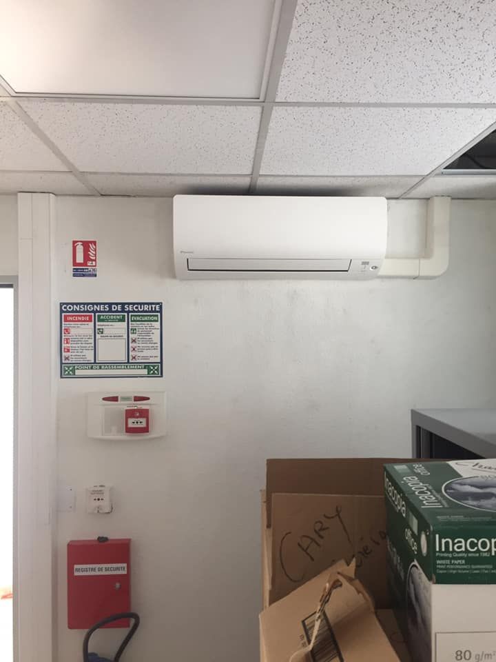 Mur intérieur d'un bureau avec un climatiseur blanc, des panneaux de sécurité, un déclencheur d'alarme incendie et un extincteur.