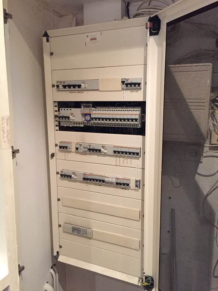 Un tableau électrique domestique avec plusieurs interrupteurs, logé dans une armoire blanche fixée au mur.